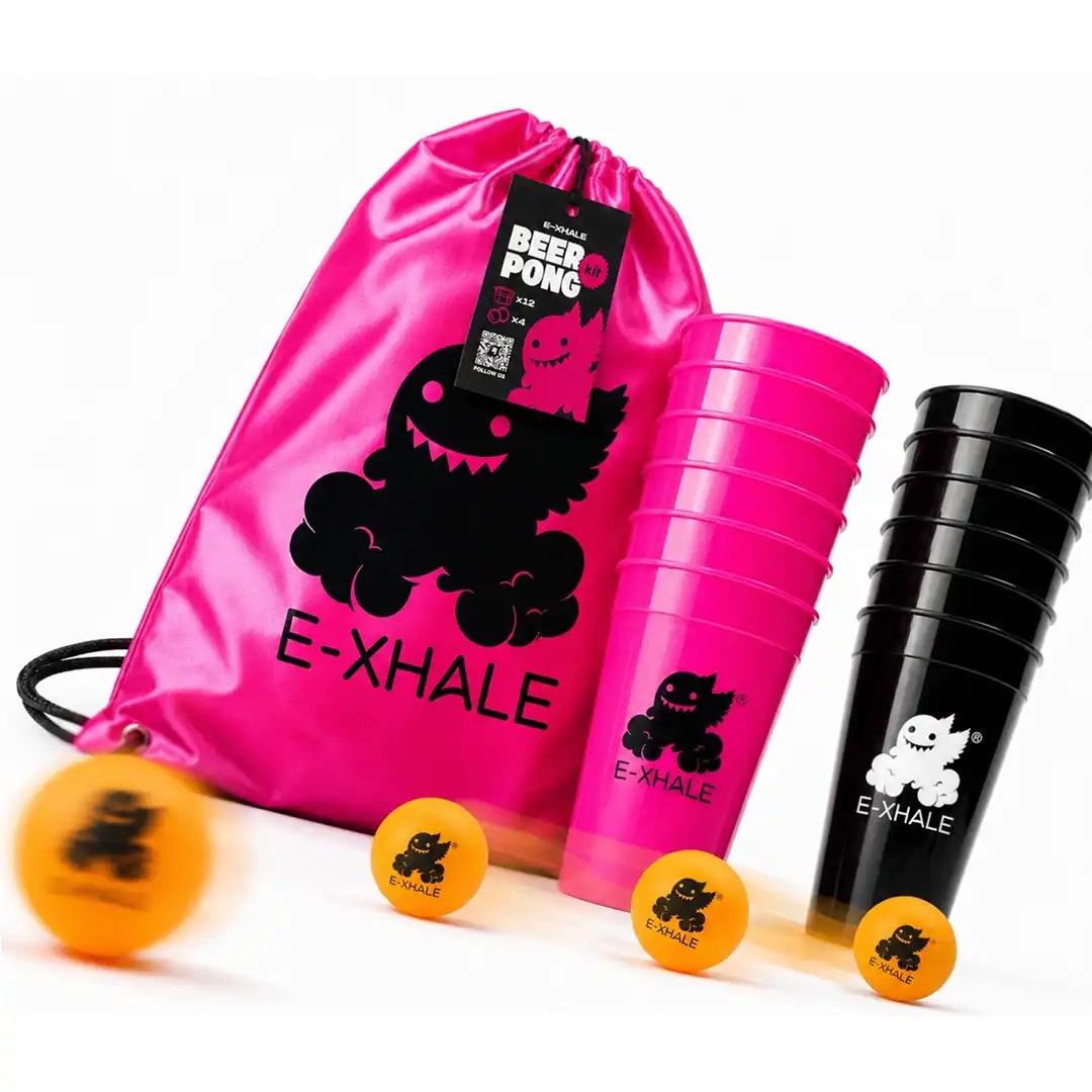 A beer pong game set on a white background, featuring a shiny pink drawstring bag with a black monster graphic and the brand name 'E-XHALE', a stack of pink cups, a stack of black cups, and orange balls.