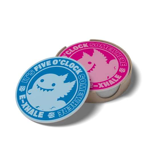 Two round printed coasters or small discs displayed on a light wood tray against a plain white background. One disc is blue with a light blue monster illustration and the text 'IT'S FIVE O'CLOCK SOMEWHERE' and 'EN-E-XHALE'.